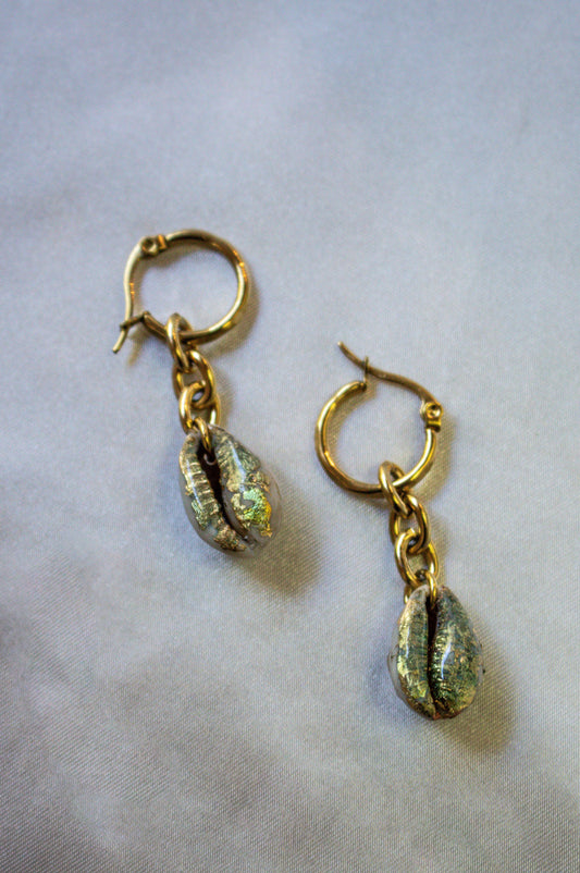 Chunky Gilded Drops earrings showcase shimmering gold and sea-green cowrie shells, perfect for a mermaid-inspired look.