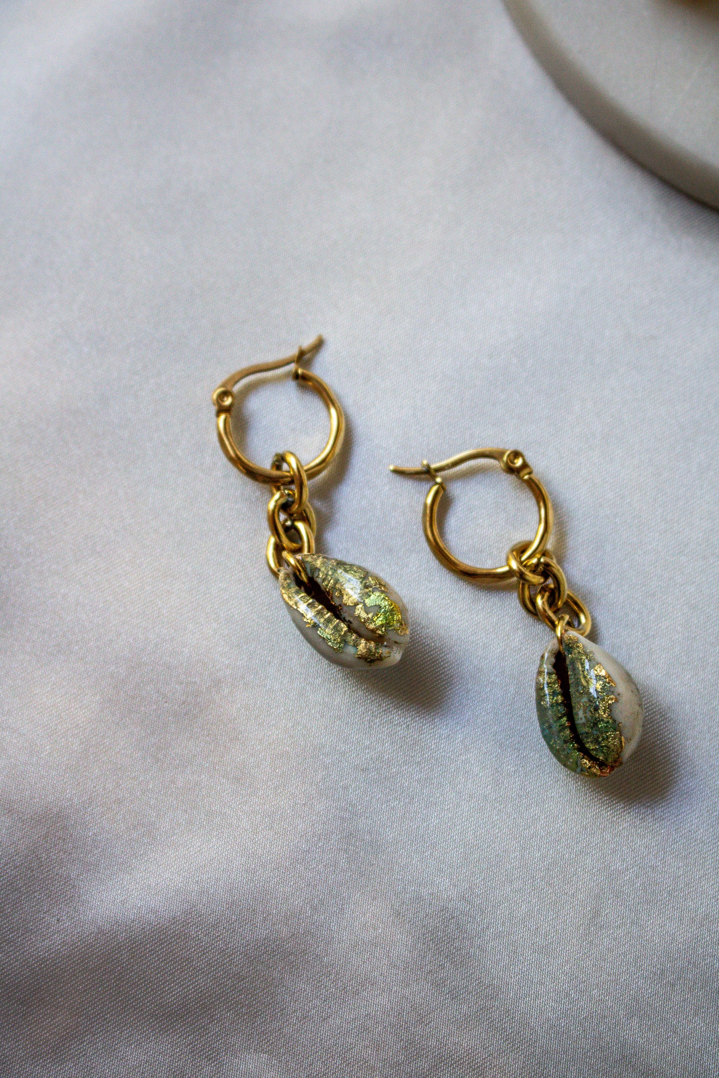 Chunky Gilded Drops earrings showcase hand-gilded cowrie shells with a shimmering gold and sea-green finish.